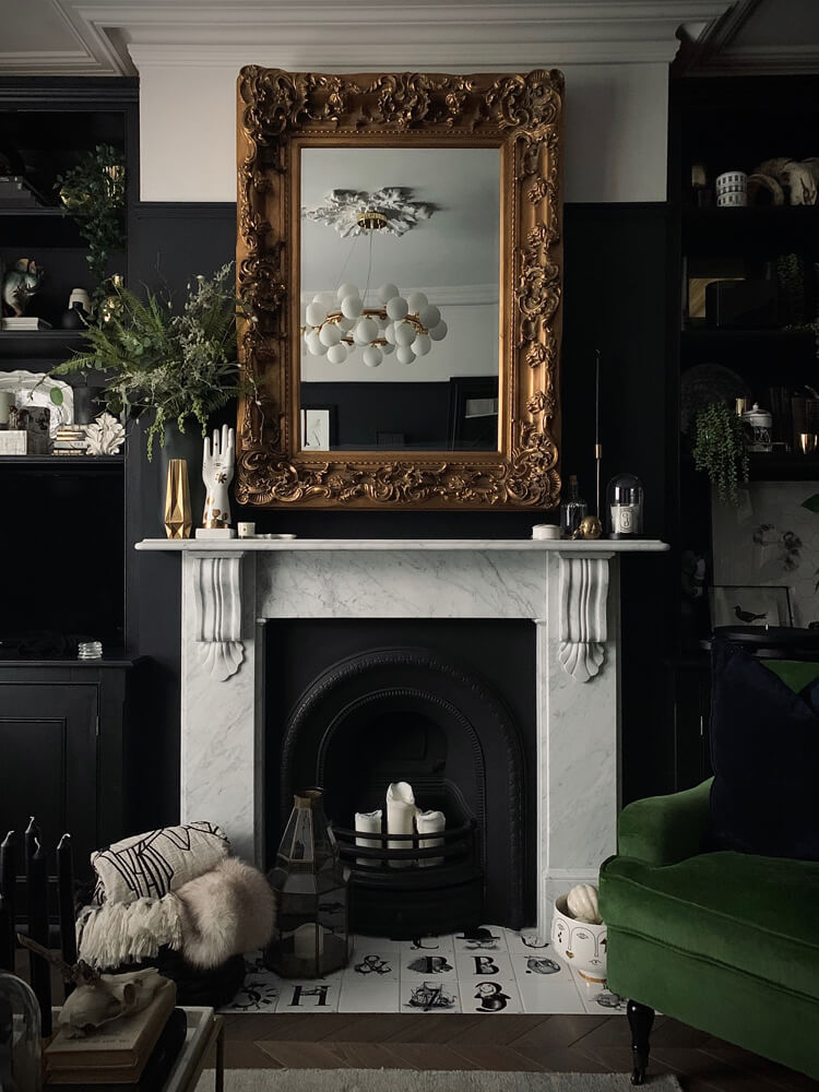 A dark and moody living room with gold mirror and green chair