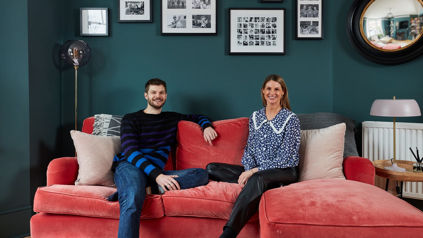 Tash and Jim Chapman sitting on a red sofa in Jim Chapman's living room painted in Lick Teal 03